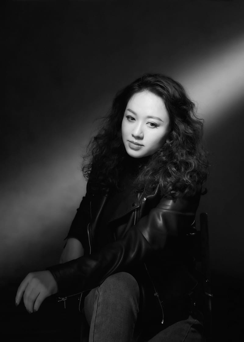 黑白肖像：穿皮衣的女性侧坐在椅边